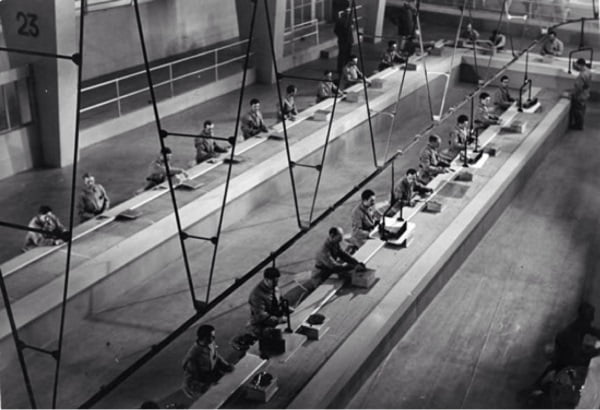 Imagem de um filme do Charlie Chaplin em que os operários trabalham na linha de produção da fábrica.